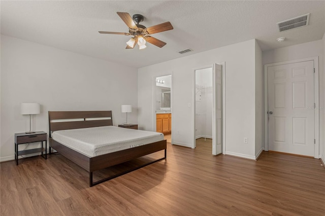 bedroom featuring ceiling fan, hardwood / wood-style flooring, ensuite bathroom, and a walk in closet