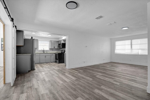 unfurnished living room with light hardwood / wood-style floors, a barn door, sink, and a textured ceiling