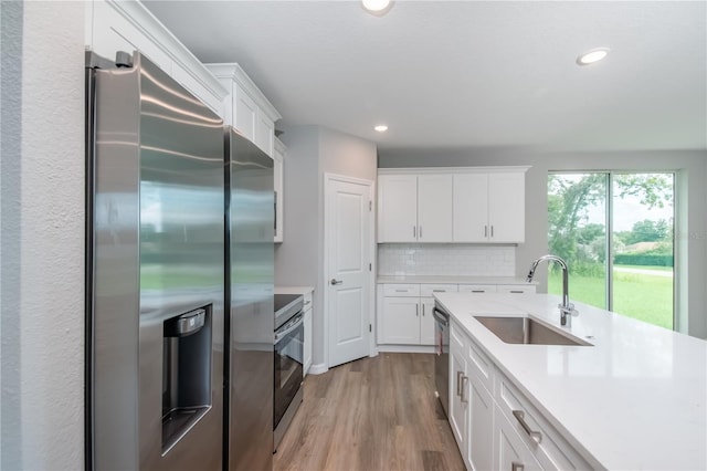 kitchen with light countertops, a sink, stainless steel appliances, light wood-style floors, and decorative backsplash