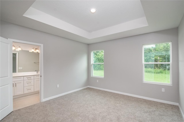 unfurnished bedroom with light carpet, baseboards, connected bathroom, and a raised ceiling