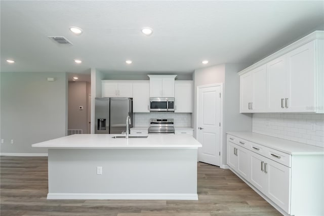kitchen featuring a sink, visible vents, white cabinets, a kitchen island with sink, and appliances with stainless steel finishes