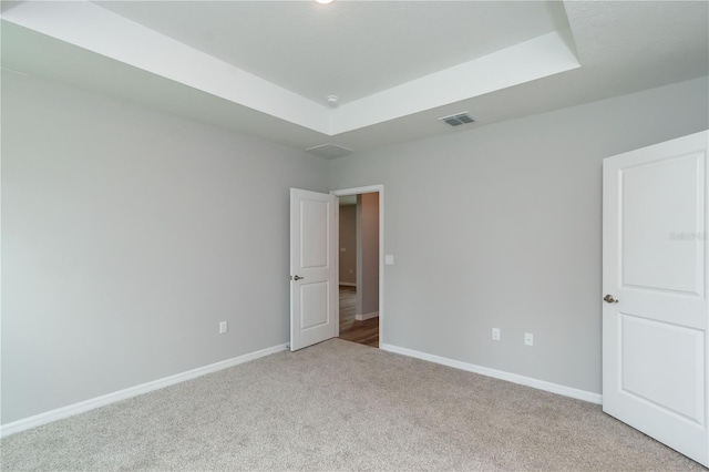 empty room with a tray ceiling, baseboards, visible vents, and carpet