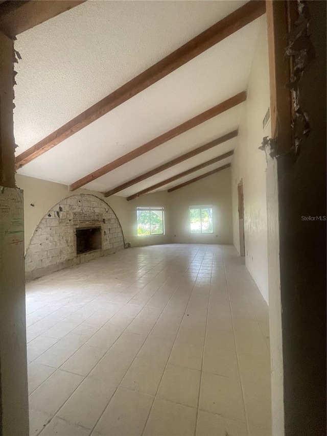 unfurnished living room with tile patterned flooring, a large fireplace, a textured ceiling, and lofted ceiling with beams