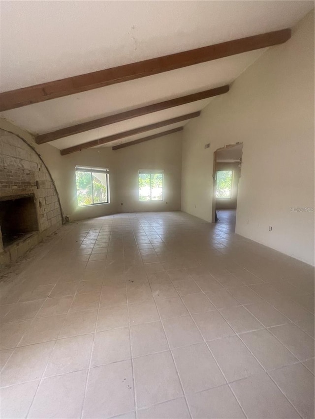 unfurnished living room with a fireplace, brick wall, light tile patterned flooring, and lofted ceiling with beams