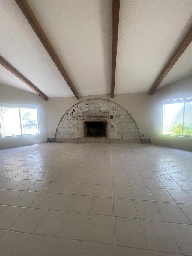 unfurnished living room with a textured ceiling, brick wall, vaulted ceiling with beams, and light tile patterned flooring