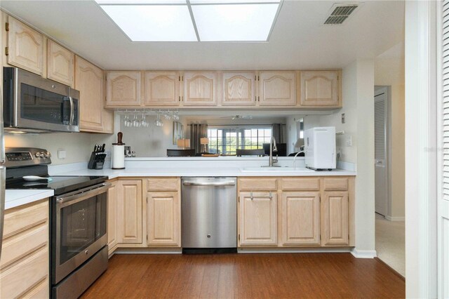 kitchen with light brown cabinets, dark hardwood / wood-style flooring, appliances with stainless steel finishes, sink, and kitchen peninsula