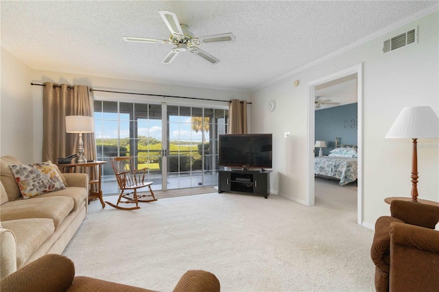 living area featuring a textured ceiling, visible vents, a ceiling fan, ornamental molding, and carpet