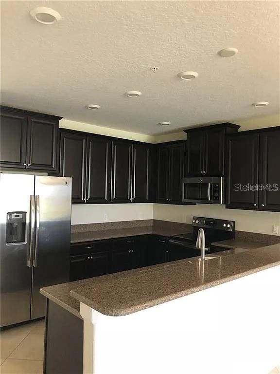 kitchen featuring dark stone countertops, a textured ceiling, appliances with stainless steel finishes, and light tile patterned floors