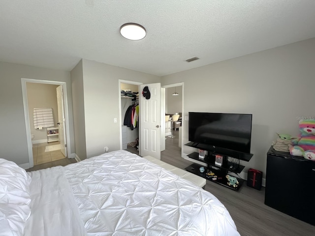 bedroom featuring a walk in closet, hardwood / wood-style flooring, a closet, connected bathroom, and a textured ceiling