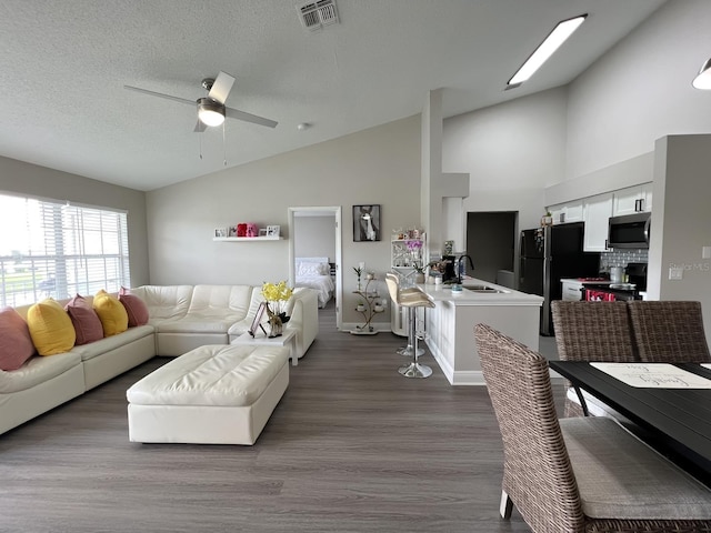 living room with sink, a textured ceiling, high vaulted ceiling, wood-type flooring, and ceiling fan