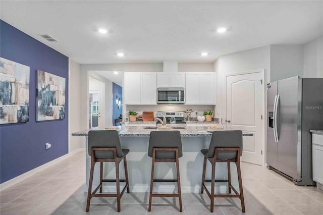 kitchen featuring light tile patterned floors, appliances with stainless steel finishes, a center island with sink, and light stone countertops