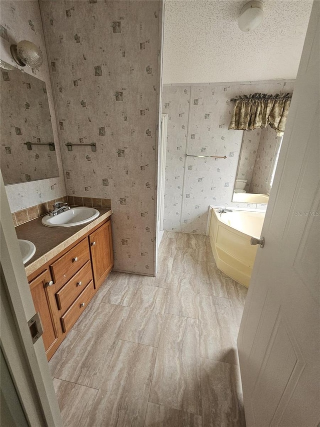 bathroom with a textured ceiling, a tub, and vanity