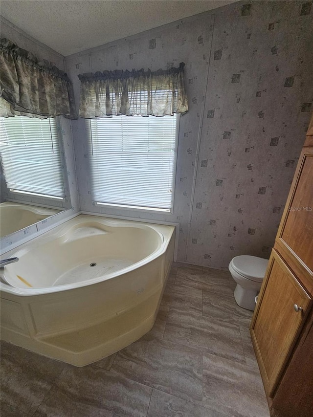 bathroom with a textured ceiling, a tub, and toilet