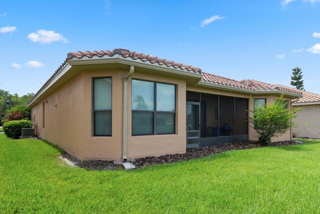 rear view of house with a lawn, a sunroom, and central AC