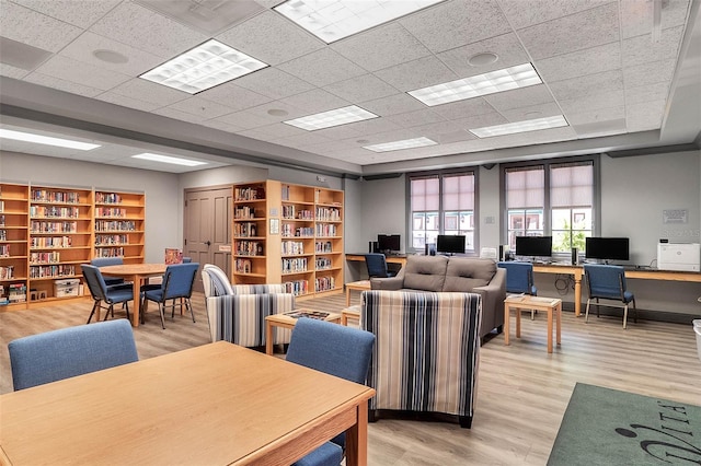 interior space featuring a drop ceiling, wall of books, and light wood finished floors