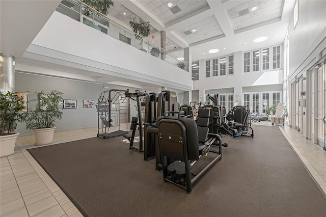 exercise room with a towering ceiling, coffered ceiling, and light tile patterned floors