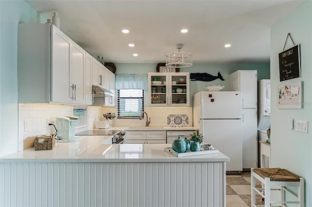 kitchen with stacked washing maching and dryer, white refrigerator, stove, light tile patterned floors, and kitchen peninsula