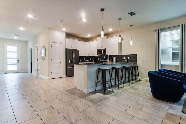 kitchen featuring white cabinetry, a kitchen bar, tasteful backsplash, black fridge with ice dispenser, and kitchen peninsula