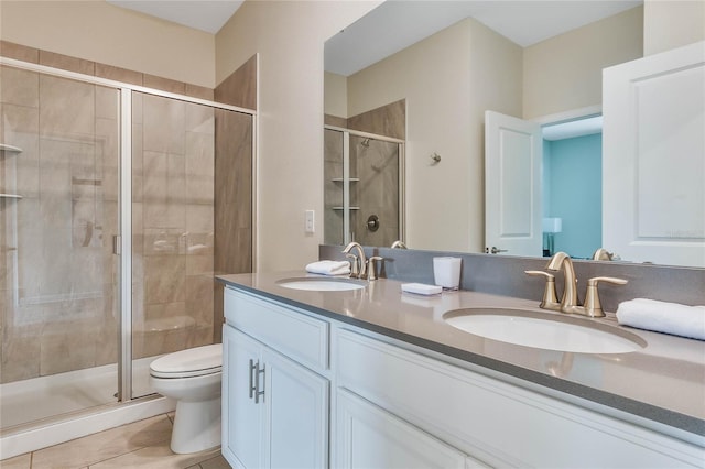 bathroom featuring toilet, dual vanity, a shower with door, and tile patterned floors