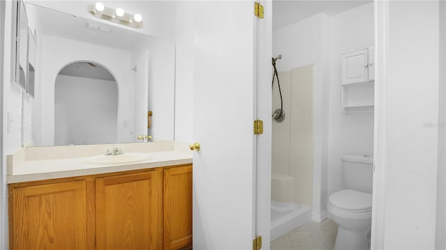 bathroom with toilet, vanity, tiled shower, and tile patterned floors