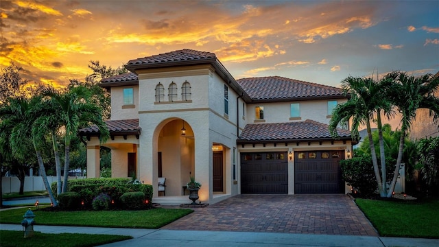 mediterranean / spanish-style home with decorative driveway, an attached garage, a tile roof, and stucco siding