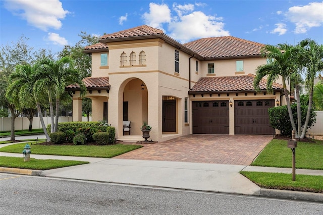 mediterranean / spanish house with decorative driveway, a tile roof, fence, and stucco siding