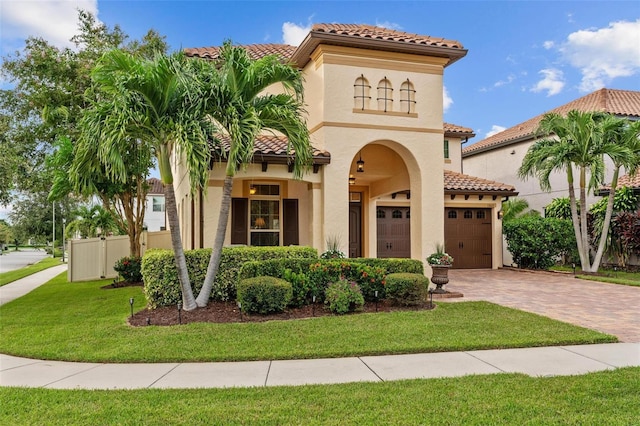 mediterranean / spanish house featuring a garage, fence, decorative driveway, stucco siding, and a front yard