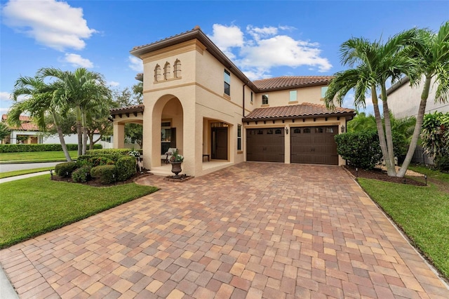 mediterranean / spanish-style home with an attached garage, a tile roof, decorative driveway, stucco siding, and a front yard