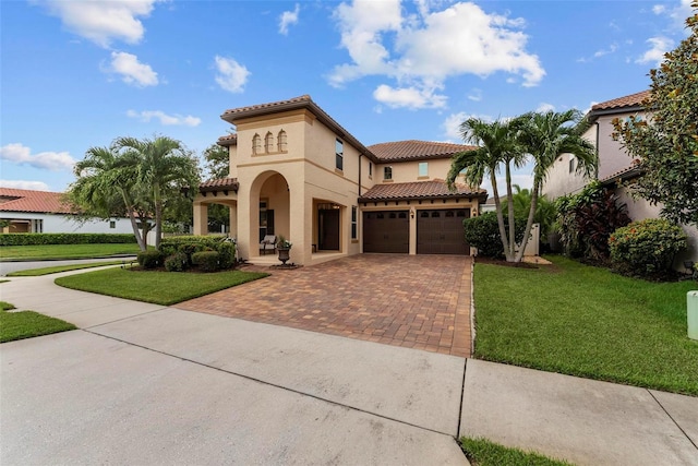 mediterranean / spanish-style home featuring decorative driveway, stucco siding, an attached garage, a tiled roof, and a front lawn