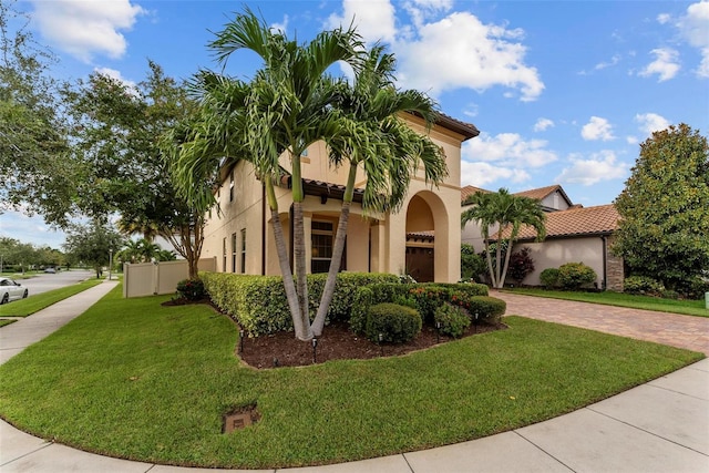 mediterranean / spanish-style house featuring a front lawn, decorative driveway, a tile roof, and stucco siding