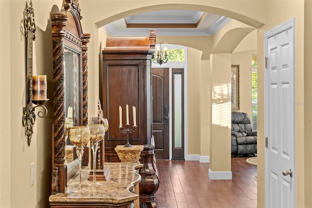 entryway with baseboards, ornamental molding, a raised ceiling, and arched walkways