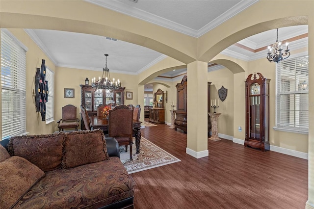 living area featuring a chandelier, arched walkways, wood finished floors, baseboards, and crown molding