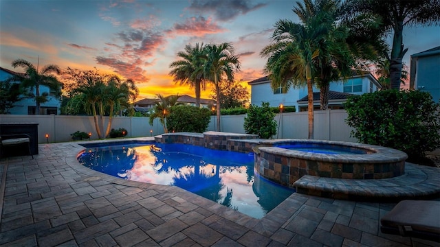 pool at dusk with an in ground hot tub and a patio area