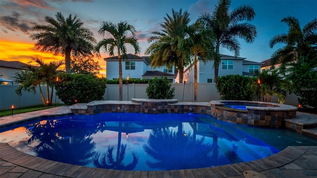 pool at dusk featuring an in ground hot tub