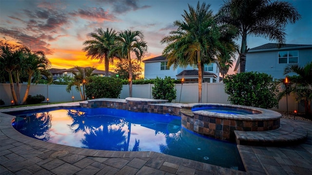 pool at dusk featuring an in ground hot tub