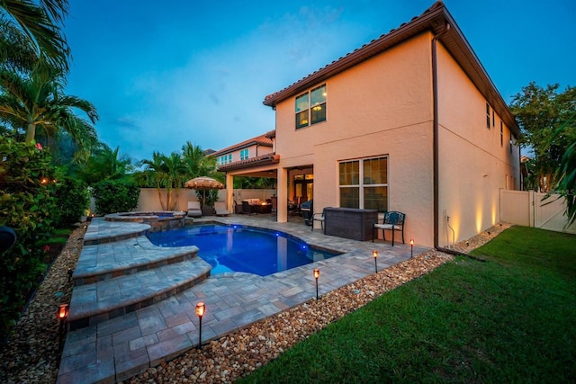 pool at dusk with a lawn, a patio area, and an in ground hot tub