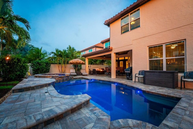 pool at dusk with an in ground hot tub and a patio area