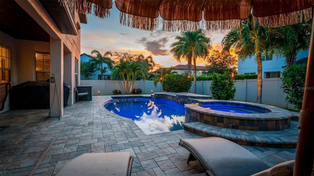 pool at dusk featuring a patio and an in ground hot tub