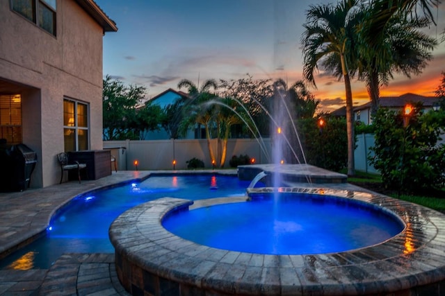 pool at dusk with pool water feature, an in ground hot tub, and area for grilling