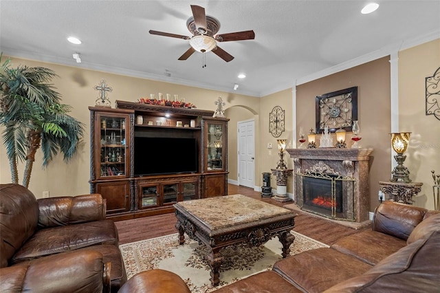 living room with ceiling fan, ornamental molding, a premium fireplace, and wood-type flooring