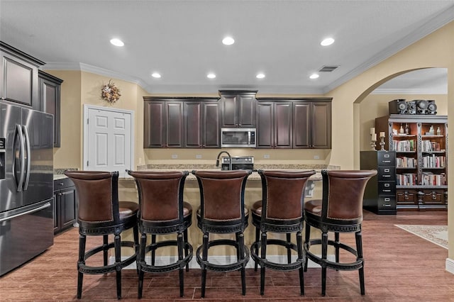 kitchen featuring hardwood / wood-style floors, stainless steel appliances, ornamental molding, and an island with sink