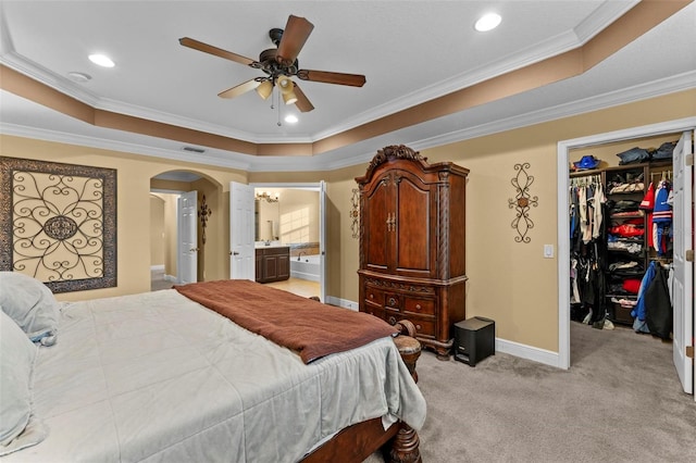 bedroom featuring ornamental molding, a closet, a tray ceiling, ceiling fan, and light colored carpet