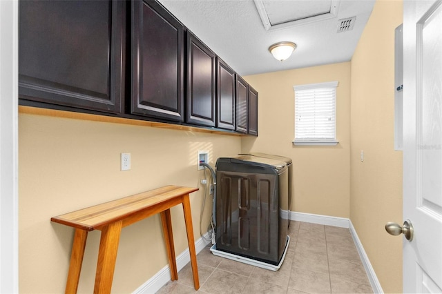 clothes washing area with washer and dryer, cabinets, and light tile patterned floors