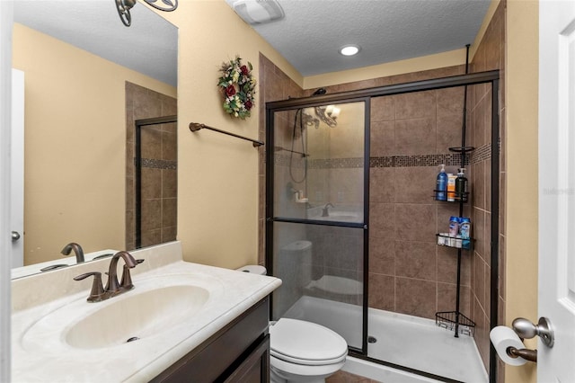 bathroom with a textured ceiling, toilet, vanity, and a shower with shower door