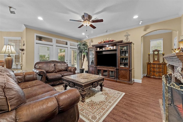 living room with ceiling fan, ornamental molding, hardwood / wood-style floors, and a stone fireplace