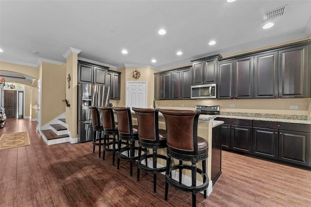 kitchen featuring appliances with stainless steel finishes, light hardwood / wood-style flooring, ornamental molding, a kitchen breakfast bar, and a kitchen island