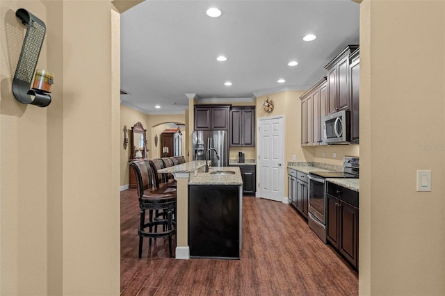 kitchen featuring arched walkways, dark wood-style floors, appliances with stainless steel finishes, a breakfast bar, and a sink