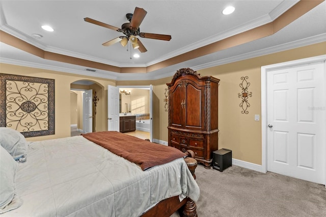 bedroom featuring crown molding, a tray ceiling, ceiling fan, light carpet, and ensuite bathroom