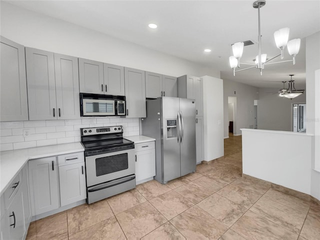 kitchen featuring gray cabinets, pendant lighting, stainless steel appliances, ceiling fan with notable chandelier, and decorative backsplash