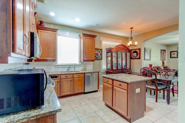 kitchen featuring appliances with stainless steel finishes, backsplash, sink, light tile patterned floors, and a center island